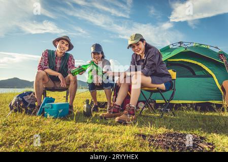 Group of travelers camping and doing picnic in meadow with tent foreground. Mountain and lake background. People and lifestyles Stock Photo