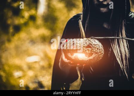 Pumpkin lantern in witch hand. Old woman holding pumpkin in dark green forest. Halloween day and Mystery concept. Fantasy of mag Stock Photo