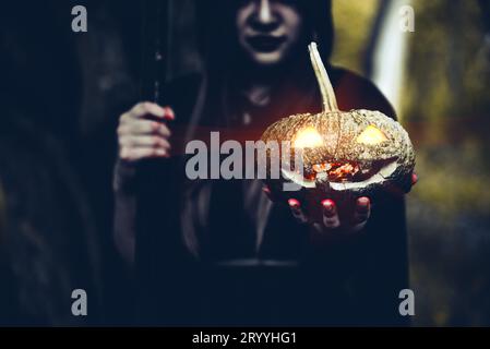 Pumpkin in witch hand. Old woman holding pumpkin in dark forest. Halloween day and Mystery concept. Fantasy of magic theme. Stock Photo