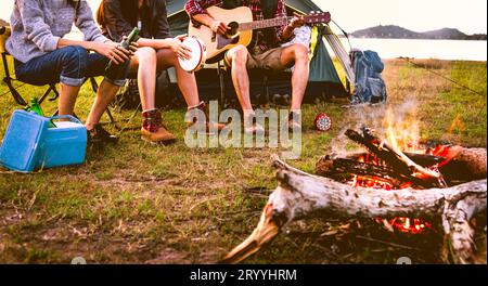 Travelers camping doing picnic and playing music in meadow field. Mountain and lake background. People and lifestyles concept. O Stock Photo