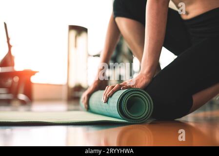 Close up of sporty woman folding yoga mattress in sport fitness gym training center background. Exercise mat rolling keeping aft Stock Photo