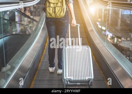 Back view of beauty woman traveling and holding suitcase on escalator in airport. People and Lifestyles concept. Travel around t Stock Photo
