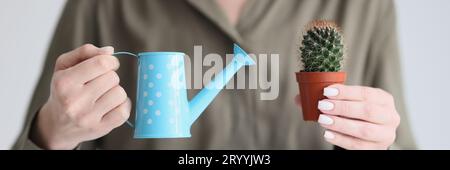Woman holds blue watering can and spiked cactus in pot Stock Photo