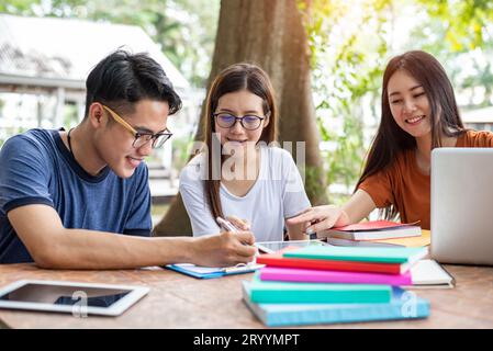 Three Asian young campus students enjoy tutoring and reading books together. Friendship and Education concept. Campus school and Stock Photo