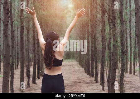 Women stretching arms and breathing fresh air in middle of pinewood forest while exercising. Workouts and Lifestyles concept. Ha Stock Photo