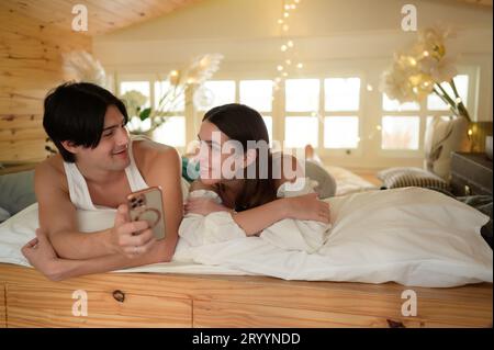 Young couple in the attic bedroom in the morning, Say hi to pals online using smartphone. Stock Photo