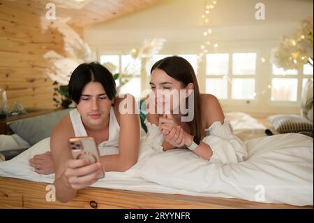 Young couple in the attic bedroom in the morning, Say hi to pals online using smartphone. Stock Photo