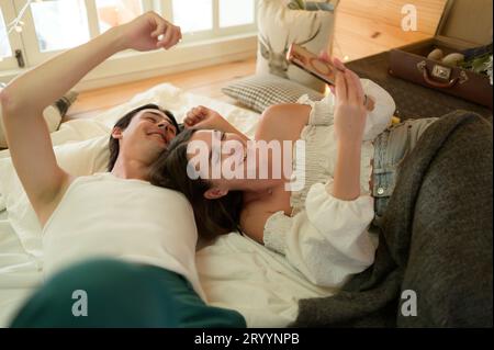 Young couple in the attic bedroom in the morning, Say hi to pals online using smartphone. Stock Photo