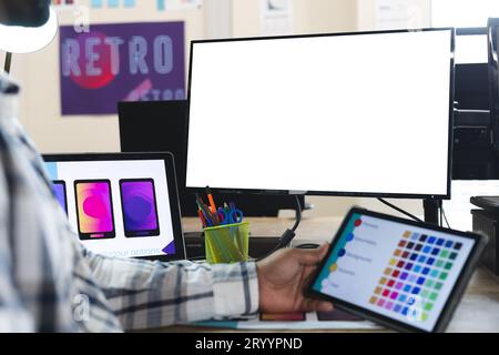 Midsection of indian male designer using tablet and computer with copy space at desk in office. Creative business, design, technology and casual offic Stock Photo