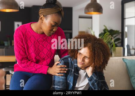 Thoughtful, sad diverse couple sitting in living room at home, embracing and comforting Stock Photo