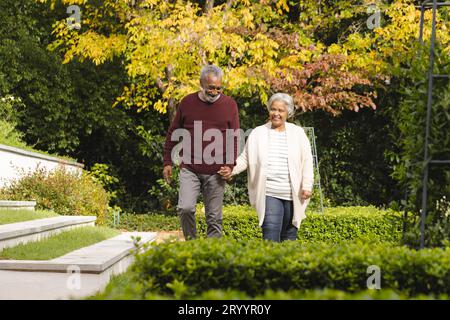 Happy senior biracial couple holding hands and walking in garden at home Stock Photo