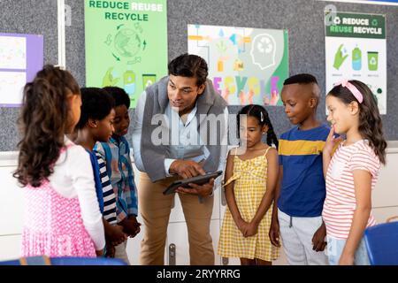 Biracial male teacher using tablet teaching children in elementary school class Stock Photo