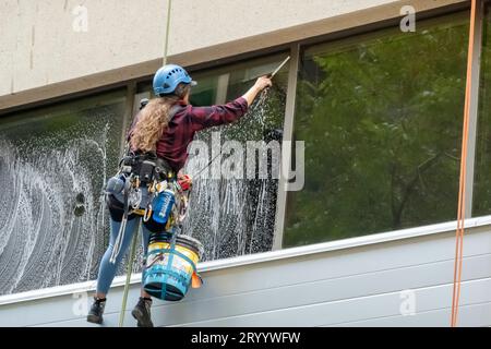 Calgary, Alberta, Canada. July 28, 2023. A female worker cleaning a window from a tall building during summer. Skyscraper Window Stock Photo