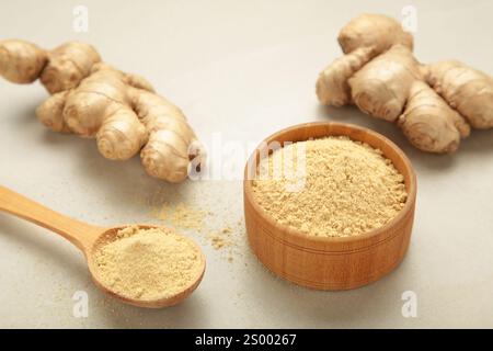 Ginger powder on bowl with fresh ginger root on light background. Stock Photo