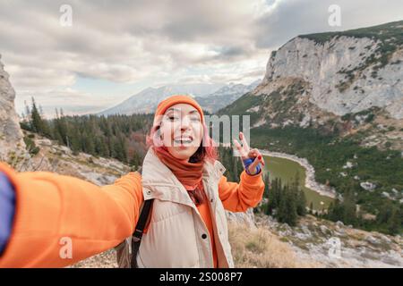 Happy hiker taking a selfie with victory gesture while enjoying the stunning mountain landscape Stock Photo