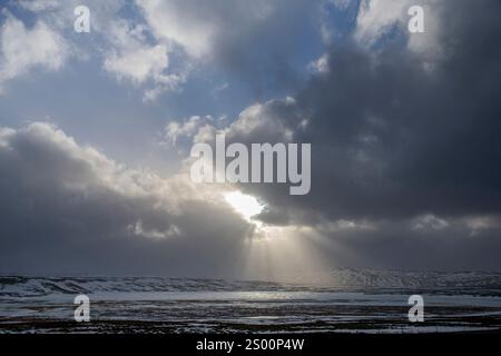 Dramatic winter landscape in Iceland with white and black clouds over snowy and icy hilly landscape with bright sun between clouds and sunrays on shin Stock Photo