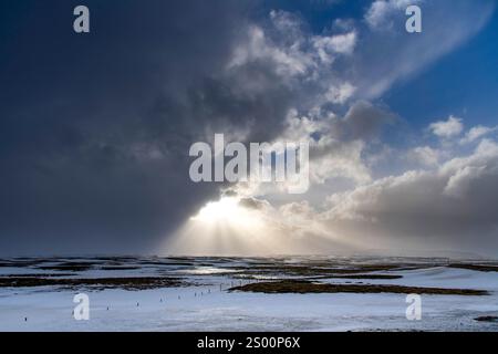 Dramatic winter landscape in Iceland with white and black clouds over snowy and icy hilly landscape with bright sun between clouds and sunrays on shin Stock Photo