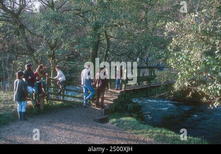 A sunshine Sunday in February finds families and other walkers crossiing a bridge over the River Dove Dovedale below Thorpe Cloud near Ashbourne Derbyshire Stock Photo