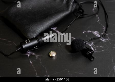 Lavalier microphone on a black background with a spare battery. Stock Photo