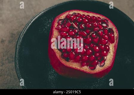Sliced fresh pomegranate, on a black plate, top view, rustic style, no people Stock Photo
