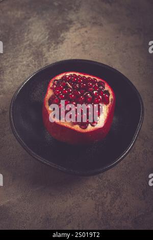 Sliced fresh pomegranate, on a black plate, top view, rustic style, no people Stock Photo