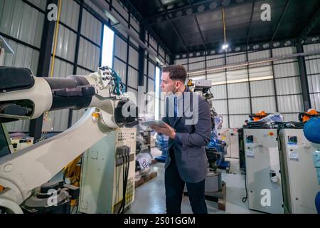 A man in professional attire examines robotic machinery in a well-lit industrial space filled with advanced equipment. The setting showcases the integ Stock Photo