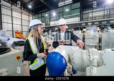Two engineers discuss a robotics project while inspecting machinery in a high-tech manufacturing facility. Stock Photo