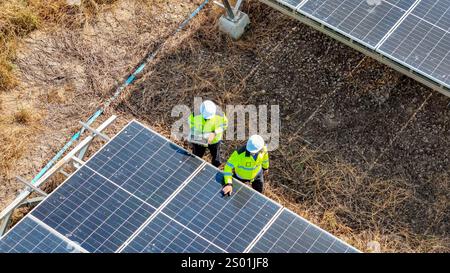Two workers in yellow vests are closely inspecting solar panels in a field. The setting is sunny, showcasing the solar installation in a largely dry l Stock Photo