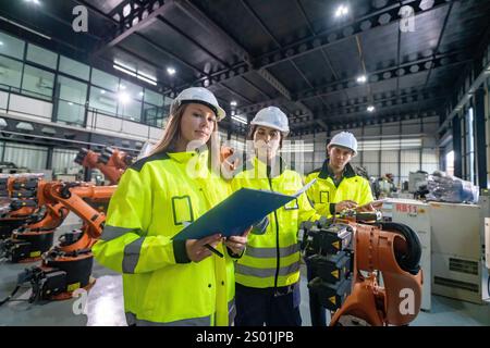 Engineers in safety gear examine project documents while surrounded by robotic arms in a high-tech manufacturing facility. The atmosphere reflects foc Stock Photo