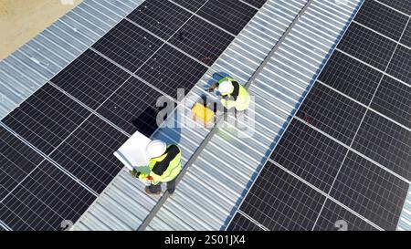 Two workers are carefully installing solar panels on a rooftop. They are equipped with safety gear, demonstrating teamwork and focus while ensuring pr Stock Photo