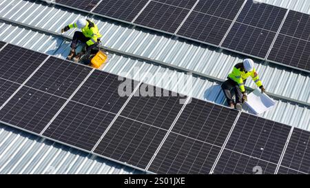 Two technicians are securely working on a roof covered with solar panels, focusing on installing or maintaining the modules under clear skies. Safety Stock Photo