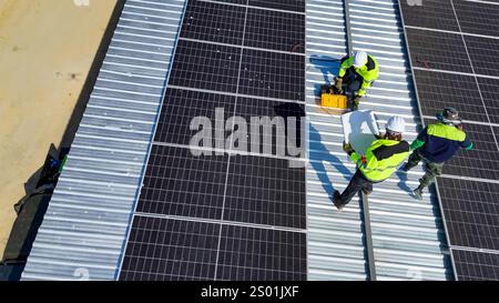 Workers are seen installing solar panels on a metal rooftop under clear blue skies in the afternoon. The innovative project promotes renewable energy Stock Photo