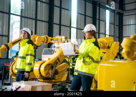 Two engineers in high-visibility jackets and helmets observe and operate advanced robotic machinery in a contemporary manufacturing environment. The f Stock Photo