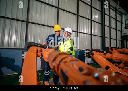 Two engineers are working together in a manufacturing facility, examining robotic machinery. They are in safety gear and focused on optimizing automat Stock Photo