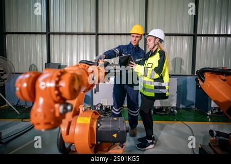 Two professionals engage in a discussion while operating an industrial robot in a modern manufacturing facility. Both wear protective gear to ensure s Stock Photo
