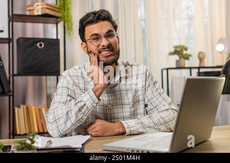 Arabian businessman freelancer working on laptop and feeling toothache touching mouth with hand, painful expression because of dental illness. Caries, pulpitis, gum disease, dental disease concepts Stock Photo