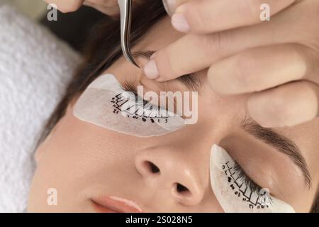 Esthetician taping woman's eyelid before lash extensions procedure in beauty salon, closeup Stock Photo