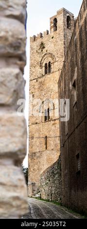 A narrow street view featuring a historic stone tower with intricate architectural details. The tower is partially obscured by a stone wall, showcasin Stock Photo