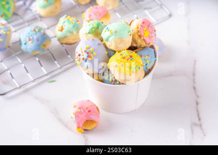 Sweet colorful glazed donuts holes dessert, mini small doughnuts with colorful glaze and sugar sprinkles, on white kitchen table Stock Photo