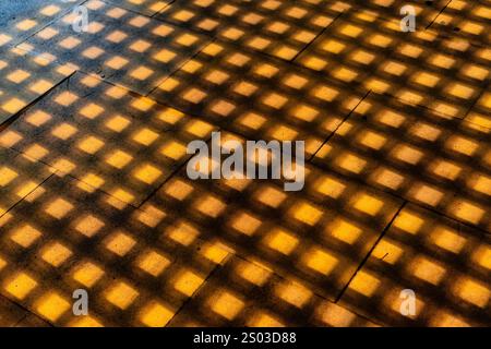 A pattern of squares on a floor, with the squares being a mix of yellow and brown. The shadows of the squares are cast on the floor, creating a sense Stock Photo