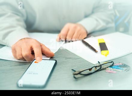 A person reviews cryptocurrency data on a smartphone and makes notes while analyzing market trends in a contemporary office environment. Stock Photo