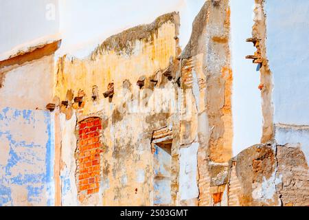 Deteriorating wall shows visible signs of decay and weathering. Wall features a mix of exposed brickwork, crumbling plaster and remnants of paint with Stock Photo