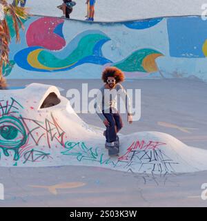 Cool young man with big hair and sun glasses on Skate Board at a Skate Park in the village of Taghazout, Morocco. Dec 23, 2024 Stock Photo
