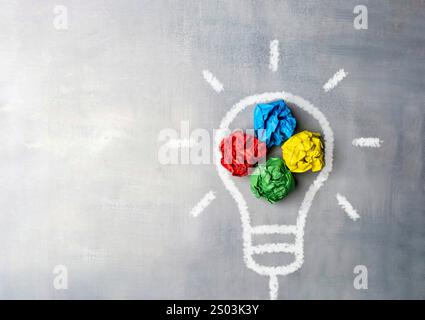 A lightbulb drawn on a chalkboard with crumpled pieces of paper in red, yellow, green, and blue. Brainstorming concept. Stock Photo