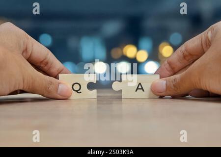A close-up image of two hands holding puzzle pieces with the letters "Q" and "A". Question and Answer concept. Stock Photo