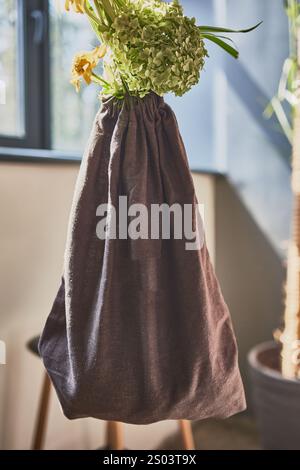 Eco-friendly fabric bag holding fresh hydrangea flowers in a bright room, representing a sustainable lifestyle concept Stock Photo