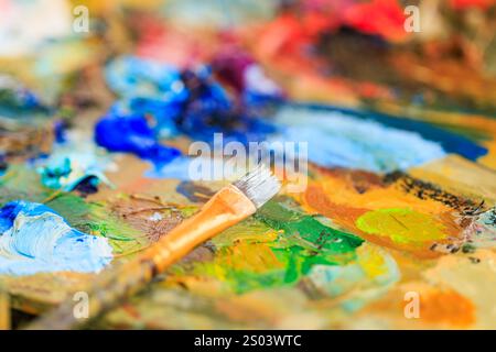 Close-up of an artist's palette covered in vibrant, colorful oil paints with a paintbrush resting on top, showcasing the creative process and artistic Stock Photo