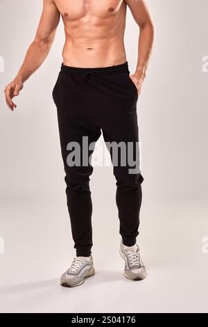 Fit man in athletic black joggers and sneakers displaying fitness fashion style in a studio setting, fitness fashion style concept Stock Photo