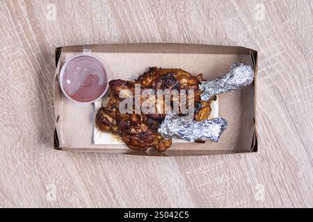 Two grilled chicken legs with sauce in a cardboard takeaway box. Stock Photo