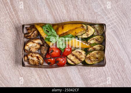 Assortment of grilled vegetables, including zucchini, peppers, mushrooms, and tomatoes, packed in a takeaway box. Stock Photo